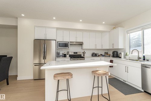 Kitchen featuring stainless steel appliances, light wood-style floors, white cabinets, a kitchen island, and a kitchen breakfast bar - 2 11569 University Avenue, Edmonton, AB - Indoor Photo Showing Kitchen With Upgraded Kitchen