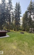 View of grassy yard with a patio area, a hot tub, a fire pit, and view of scattered trees - 