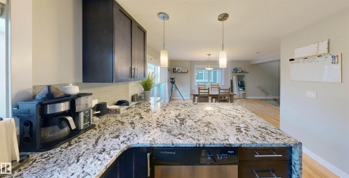 Kitchen with dark wood finish cabinetry, light stone counters, hanging light fixtures, dishwasher, and decorative backsplash - 8 9535 217 Street, Edmonton, AB - Indoor Photo Showing Kitchen With Upgraded Kitchen