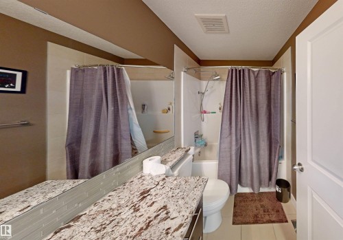 Full bath featuring a textured ceiling, shower / bath combo with shower curtain, light tile patterned floors, and vanity - 8 9535 217 Street, Edmonton, AB - Indoor Photo Showing Bathroom