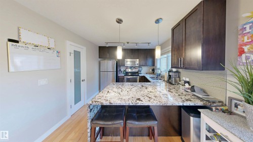 Kitchen featuring dark wood finish cabinets, a breakfast bar area, light stone counters, a peninsula, and stainless steel appliances - 8 9535 217 Street, Edmonton, AB - Indoor Photo Showing Kitchen With Upgraded Kitchen