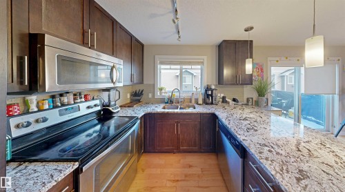 Kitchen with stainless steel appliances, dark wood finish cabinetry, light stone counters, light wood-type flooring, and decorative backsplash - 8 9535 217 Street, Edmonton, AB - Indoor Photo Showing Kitchen With Stainless Steel Kitchen With Double Sink