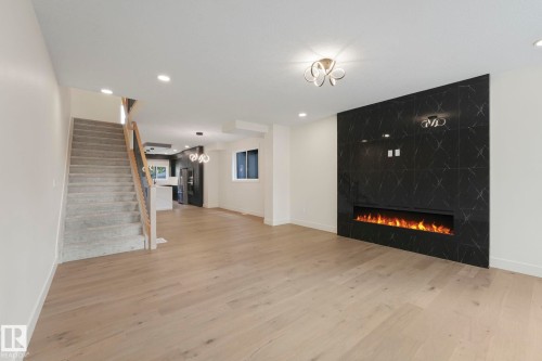 Stairway from living room featuring a fireplace, light wood finished floors, recessed lighting, stairway, and a chandelier - 10965 129 Street, Edmonton, AB - Indoor With Fireplace