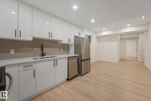 Kitchen featuring white cabinets, light wood-type flooring, recessed lighting, appliances with stainless steel finishes, and decorative backsplash - 10965 129 Street, Edmonton, AB - Indoor Photo Showing Kitchen With Double Sink