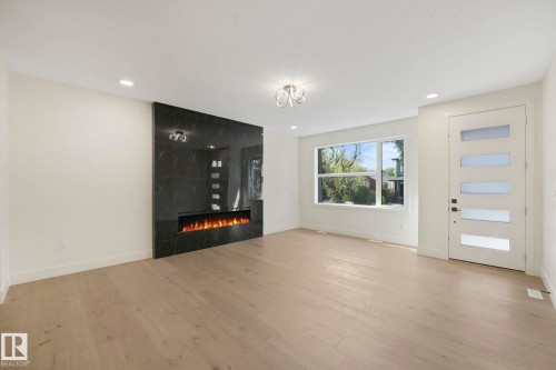 Unfurnished living room featuring light wood-style flooring and a premium fireplace - 10965 129 Street, Edmonton, AB - Indoor With Fireplace
