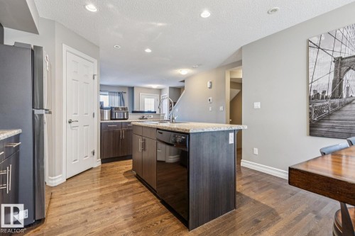Kitchen featuring freestanding refrigerator, a kitchen island with sink, dishwasher, dark wood-style floors, and dark wood finish cabinetry - 5409 3 Avenue, Edmonton, AB - Indoor Photo Showing Kitchen