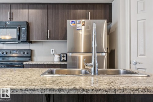 Kitchen featuring dark wood finish cabinetry, black appliances, light stone counters, and modern cabinets - 5409 3 Avenue, Edmonton, AB - Indoor Photo Showing Kitchen With Double Sink With Upgraded Kitchen