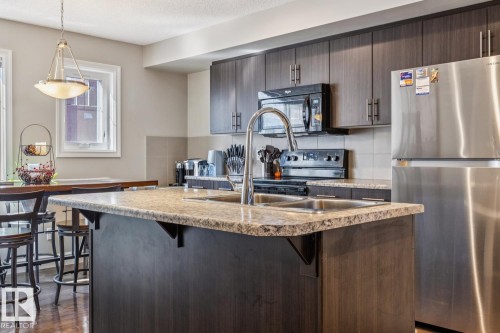 Kitchen with freestanding refrigerator, dark wood finish cabinets, a breakfast bar area, a kitchen island with sink, and tasteful backsplash - 5409 3 Avenue, Edmonton, AB - Indoor Photo Showing Kitchen With Double Sink With Upgraded Kitchen