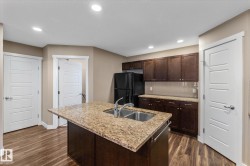 Kitchen featuring dark brown cabinets, freestanding refrigerator, dark wood-style flooring, light stone counters, and recessed lighting - 