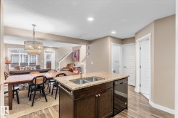 Kitchen featuring dark brown cabinetry, light stone counters, hanging light fixtures, open floor plan, and a kitchen island with sink - 