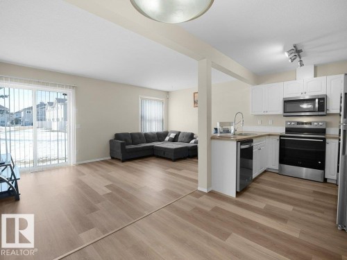 Kitchen featuring open floor plan, stainless steel appliances, white cabinetry, light wood finished floors, and rail lighting - 196 230 Edwards Drive, Edmonton, AB - Indoor Photo Showing Kitchen With Double Sink