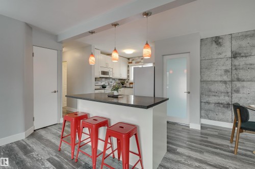 Kitchen featuring a breakfast bar, decorative light fixtures, white cabinetry, white appliances, and dark countertops - 13932 118 Avenue, Edmonton, AB - Indoor Photo Showing Kitchen