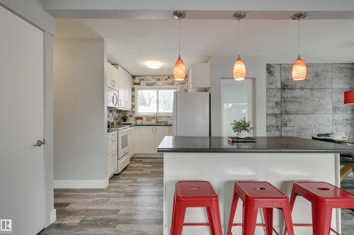 Kitchen with a breakfast bar area, white cabinetry, white appliances, hanging light fixtures, and a center island - 13932 118 Avenue, Edmonton, AB - Indoor Photo Showing Other Room