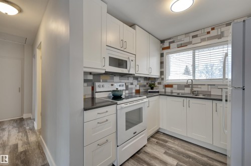 Kitchen with white appliances, light wood-style floors, decorative backsplash, and white cabinetry - 13932 118 Avenue, Edmonton, AB - Indoor Photo Showing Kitchen With Double Sink
