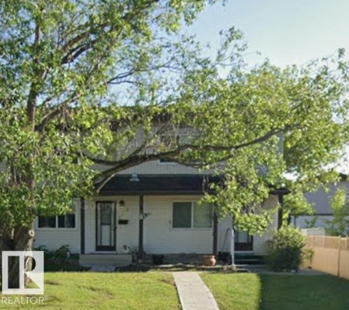 The property features a traditional exterior with light-colored siding, a dark roof, and a mature tree providing natural shading - 5404 146 Avenue Nw, Edmonton, AB - Outdoor