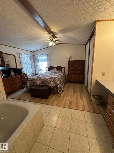 This property features a room with a ceiling fan, a prominent wooden beam, and a large window - 67 4204 47 Street, Wetaskiwin, AB - Indoor Photo Showing Bedroom