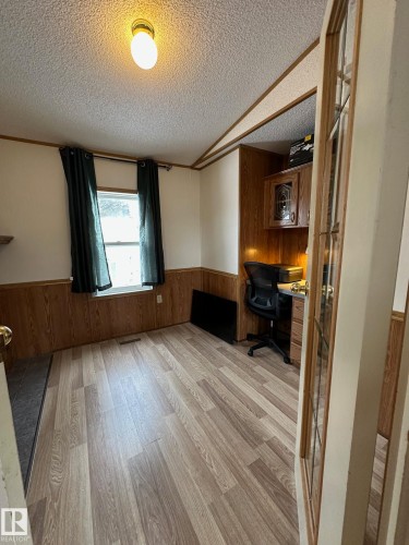 This area features light-toned flooring, a window with dark curtains, and wood paneling on the lower half of the walls - 67 4204 47 Street, Wetaskiwin, AB - Indoor Photo Showing Other Room