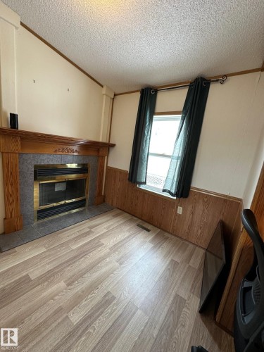 This space features a fireplace with a wood mantel and tile surround, alongside light-toned plank flooring - 67 4204 47 Street, Wetaskiwin, AB - Indoor Photo Showing Living Room With Fireplace