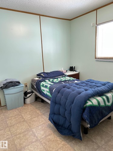 This room features light-toned walls with visible vertical accents, a window with blinds, and light-colored tile flooring - 67 4204 47 Street, Wetaskiwin, AB - Indoor Photo Showing Bedroom