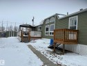 The property features a green exterior with white trim windows, an elevated wooden deck with railings, and a separate storage shed in the yard - 67 4204 47 Street, Wetaskiwin, AB  - Outdoor With Deck Patio Veranda 