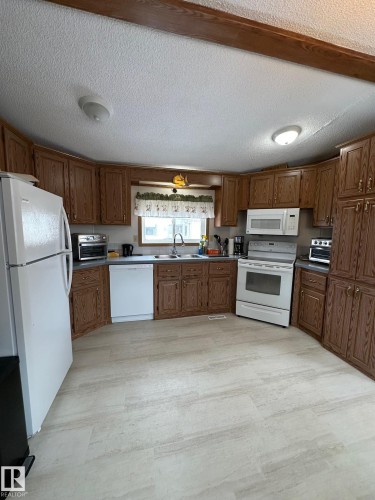Spacious kitchen featuring extensive wood cabinetry, white appliances, and light-colored flooring - 67 4204 47 Street, Wetaskiwin, AB - Indoor Photo Showing Kitchen With Double Sink