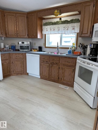 Kitchen featuring light-colored flooring, oak cabinetry, and a window above a double basin sink - 67 4204 47 Street, Wetaskiwin, AB - Indoor Photo Showing Kitchen With Double Sink