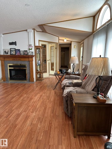 Living space featuring wood-look flooring, a fireplace with a stone surround and wooden mantel, and a window with an arched top - 67 4204 47 Street, Wetaskiwin, AB - Indoor Photo Showing Living Room With Fireplace