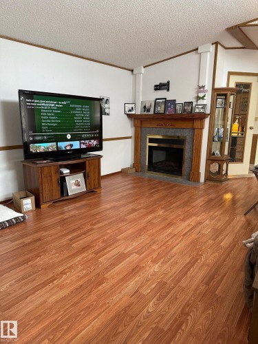 Living area featuring wood flooring, a fireplace with a wood mantle and stone surround, and white walls with wood trim - 67 4204 47 Street, Wetaskiwin, AB - Indoor Photo Showing Living Room With Fireplace