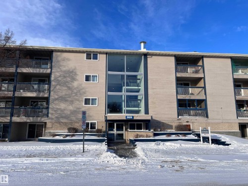 The property features a multi-story exterior with balconies, large windows, and a prominent glass-enclosed central entrance - 212 2620 Mill Woods Road E, Edmonton, AB - Outdoor With Balcony