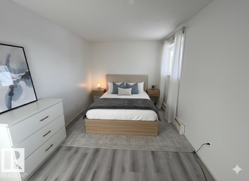 This room features light-toned flooring, white walls, and a window with sheer curtains - 212 2620 Mill Woods Road E, Edmonton, AB - Indoor Photo Showing Bedroom
