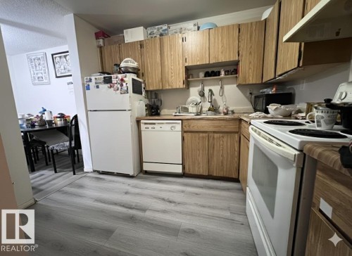 Kitchen featuring wood-look cabinetry, a white refrigerator, a white dishwasher, and gray wood-look flooring - 212 2620 Mill Woods Road E, Edmonton, AB - Indoor Photo Showing Kitchen