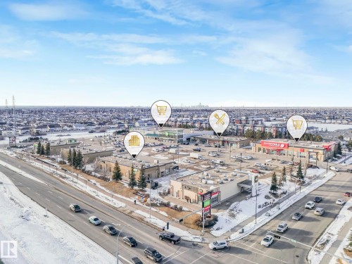 This aerial view showcases a vibrant commercial area with several businesses, ample parking spaces, and direct access to a main road - 1920 24 Street, Edmonton, AB - Outdoor With View
