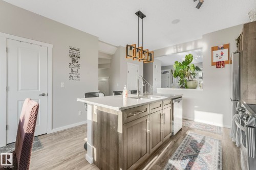 The kitchen features a central island with a sink, light-colored countertops, and wood-toned cabinetry - 1920 24 Street, Edmonton, AB - Indoor Photo Showing Kitchen