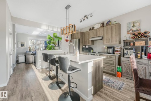 The kitchen features wood-look cabinetry, a light-colored island with a sink, and track lighting - 1920 24 Street, Edmonton, AB - Indoor Photo Showing Kitchen