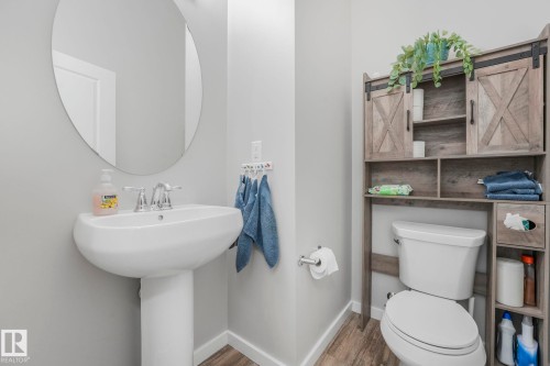 This space features a pedestal sink with chrome fixtures and an oval mirror, complemented by an over-the-toilet storage unit with barn-door style accents and open shelving - 1920 24 Street, Edmonton, AB - Indoor Photo Showing Bathroom