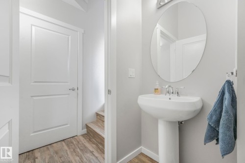 Bathroom featuring a white pedestal sink with a chrome faucet and an oval mirror, complemented by light grey walls and wood-look flooring - 1920 24 Street, Edmonton, AB - Indoor Photo Showing Bathroom