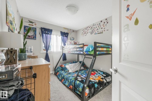 Bedroom featuring light-colored walls, grey carpeting, and a window with blue curtains - 1920 24 Street, Edmonton, AB - Indoor Photo Showing Bedroom