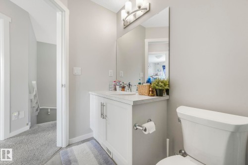 This bathroom features a white vanity with a light-colored countertop, a vanity mirror with overhead lighting, and a white toilet - 1920 24 Street, Edmonton, AB - Indoor Photo Showing Bathroom