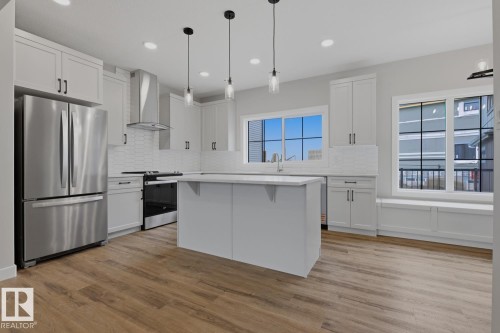 Contemporary kitchen featuring light-toned cabinetry, stainless steel appliances, a central island, wood-finish flooring, and multiple windows with an integrated window seat - 30 Chartres Close Nw, St. Albert, AB 