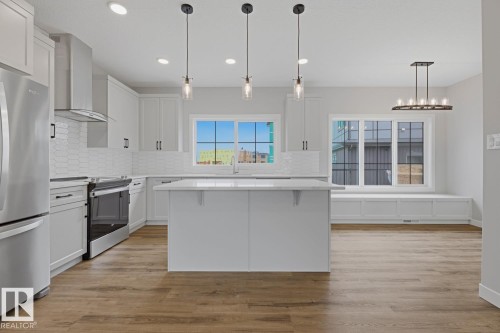 Bright kitchen featuring a central island with countertop seating, stainless steel appliances, white cabinetry, and wood-finish flooring - 30 Chartres Close Nw, St. Albert, AB 