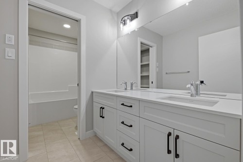 Dual vanity with white cabinetry and dark hardware, integrated sinks, and a full-width mirror - 30 Chartres Close Nw, St. Albert, AB 
