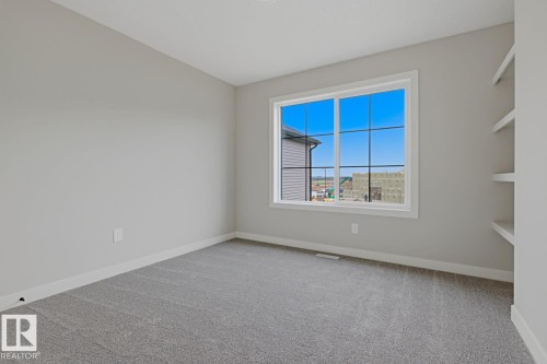 Spacious room featuring light gray walls, gray carpeting, a large white-framed window with grid panes, and built-in white shelving - 30 Chartres Close Nw, St. Albert, AB 