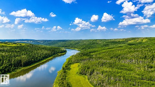 Expansive natural landscape featuring a winding river, dense green forests, and rolling grassy hills under a clear blue sky with white clouds - Rge Rd 102 Twp Rd 552A, Rural St. Paul County, AB 