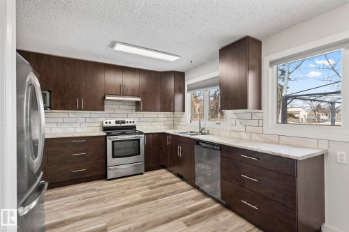 This kitchen features dark wood cabinetry, light-colored countertops, a white subway tile backsplash, and stainless steel appliances - 18124 68Ave, Edmonton, AB - Indoor Photo Showing Kitchen With Double Sink With Upgraded Kitchen