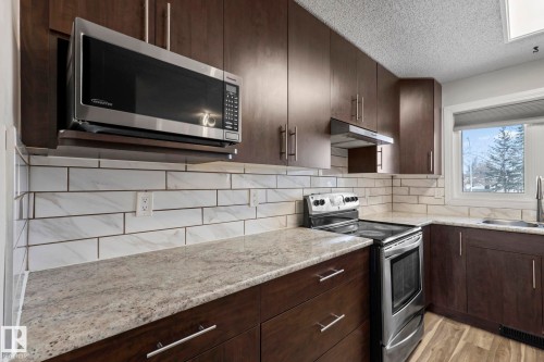 The kitchen features dark wood cabinetry, granite countertops, and a subway tile backsplash - 18124 68Ave, Edmonton, AB - Indoor Photo Showing Kitchen With Upgraded Kitchen