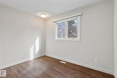 This room features rich wood-look flooring, neutral wall tones, and a window with a view of trees - 18124 68Ave, Edmonton, AB - Indoor Photo Showing Other Room