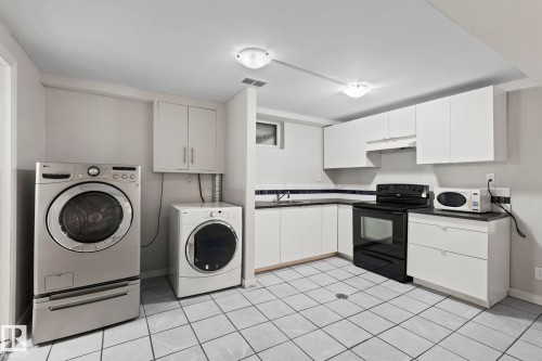 The property features a kitchen area with white cabinetry, a black range, and a microwave - 18124 68Ave, Edmonton, AB - Indoor Photo Showing Laundry Room