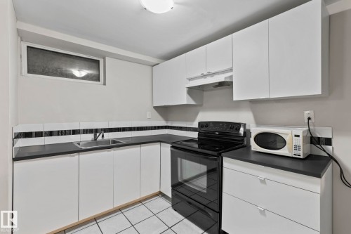The kitchen features white cabinetry, dark countertops, a tile backsplash, and a window - 18124 68Ave, Edmonton, AB - Indoor Photo Showing Kitchen