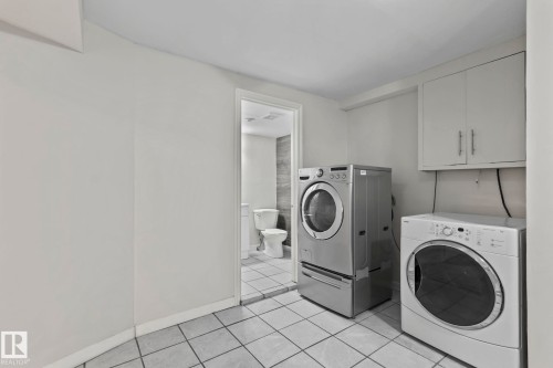 Laundry area featuring tile flooring, wall-mounted cabinetry, and a washer and dryer - 18124 68Ave, Edmonton, AB - Indoor Photo Showing Laundry Room