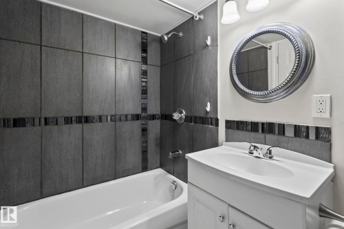 Bathroom featuring a white vanity with an integrated sink, a large framed mirror, and a bathtub with dark tiled walls - 18124 68Ave, Edmonton, AB - Indoor Photo Showing Bathroom